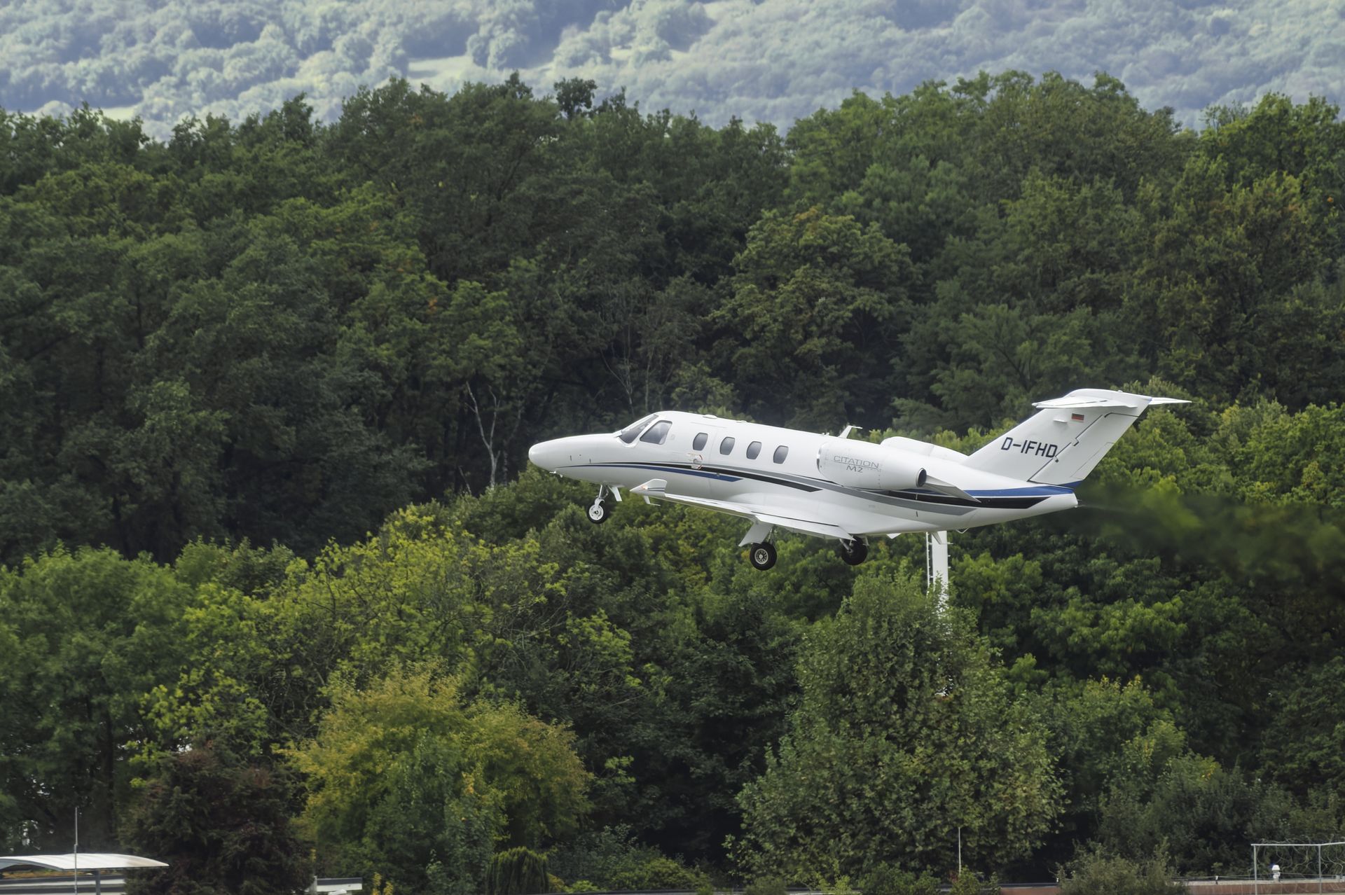 White airplane landing near a line of green trees on a sunny day.