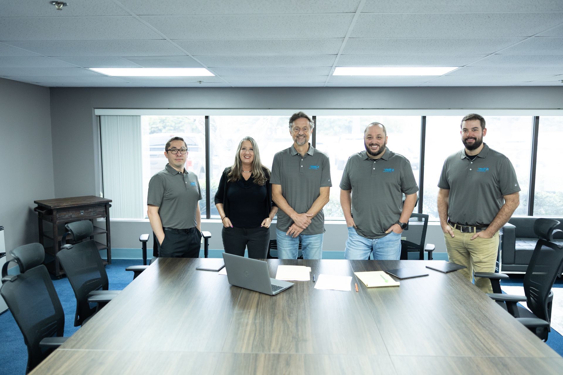 Five people stand behind a conference table in an office, looking at the camera.