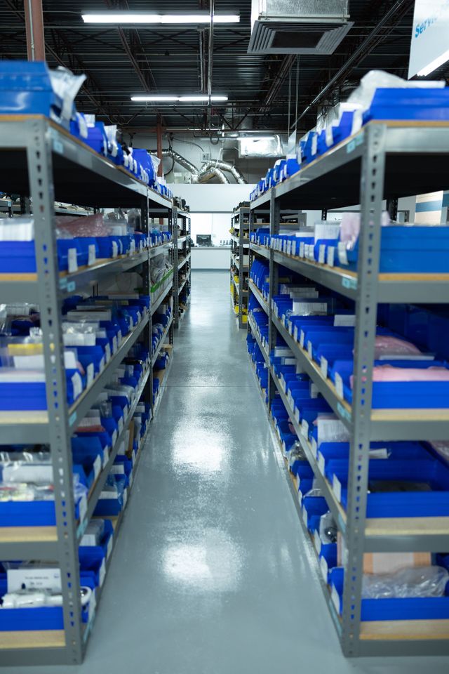 Rows of metal shelves filled with blue bins in a well-lit warehouse aisle.