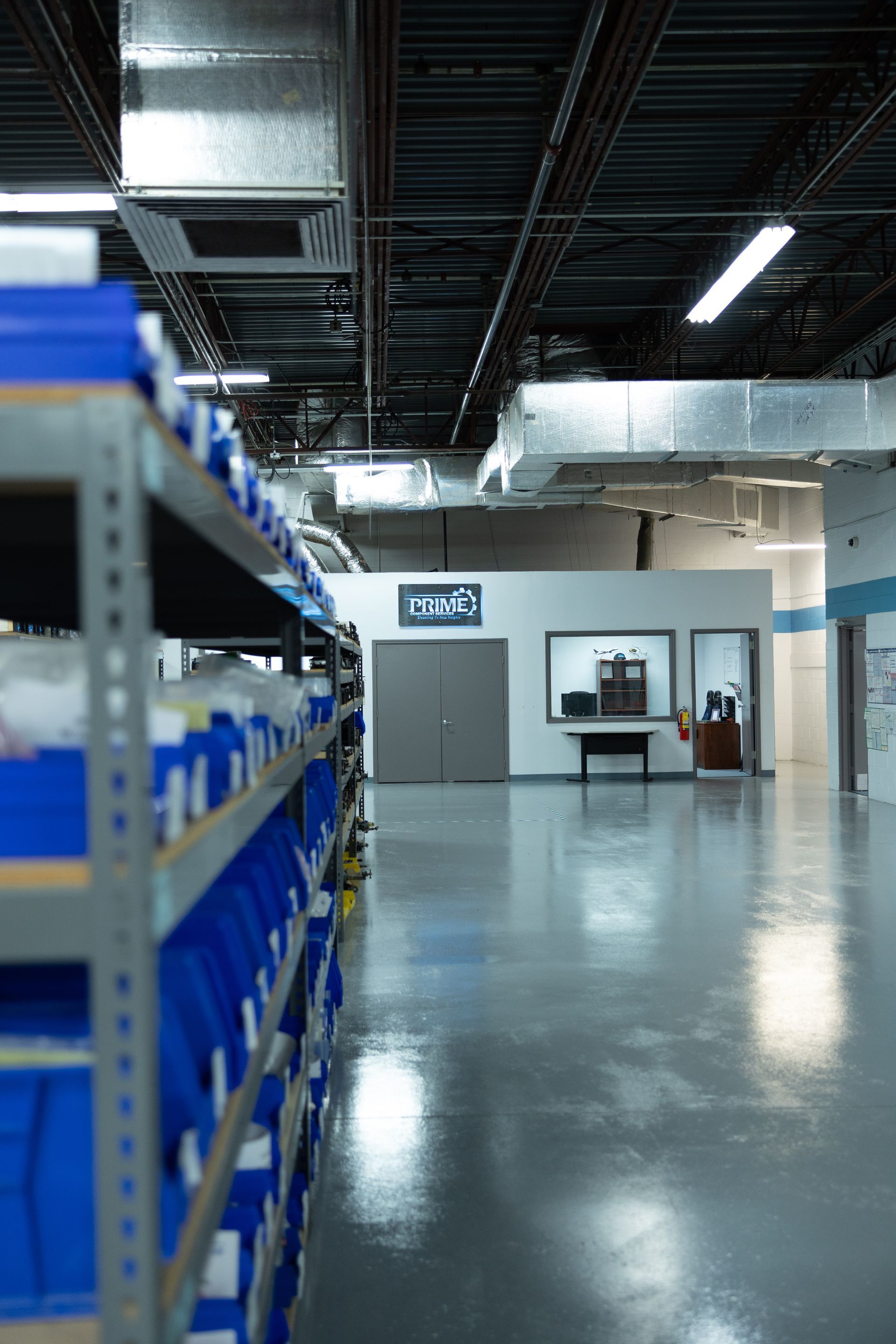 Shelving with blue bins in a warehouse setting; a door and workspace are visible in the distance.