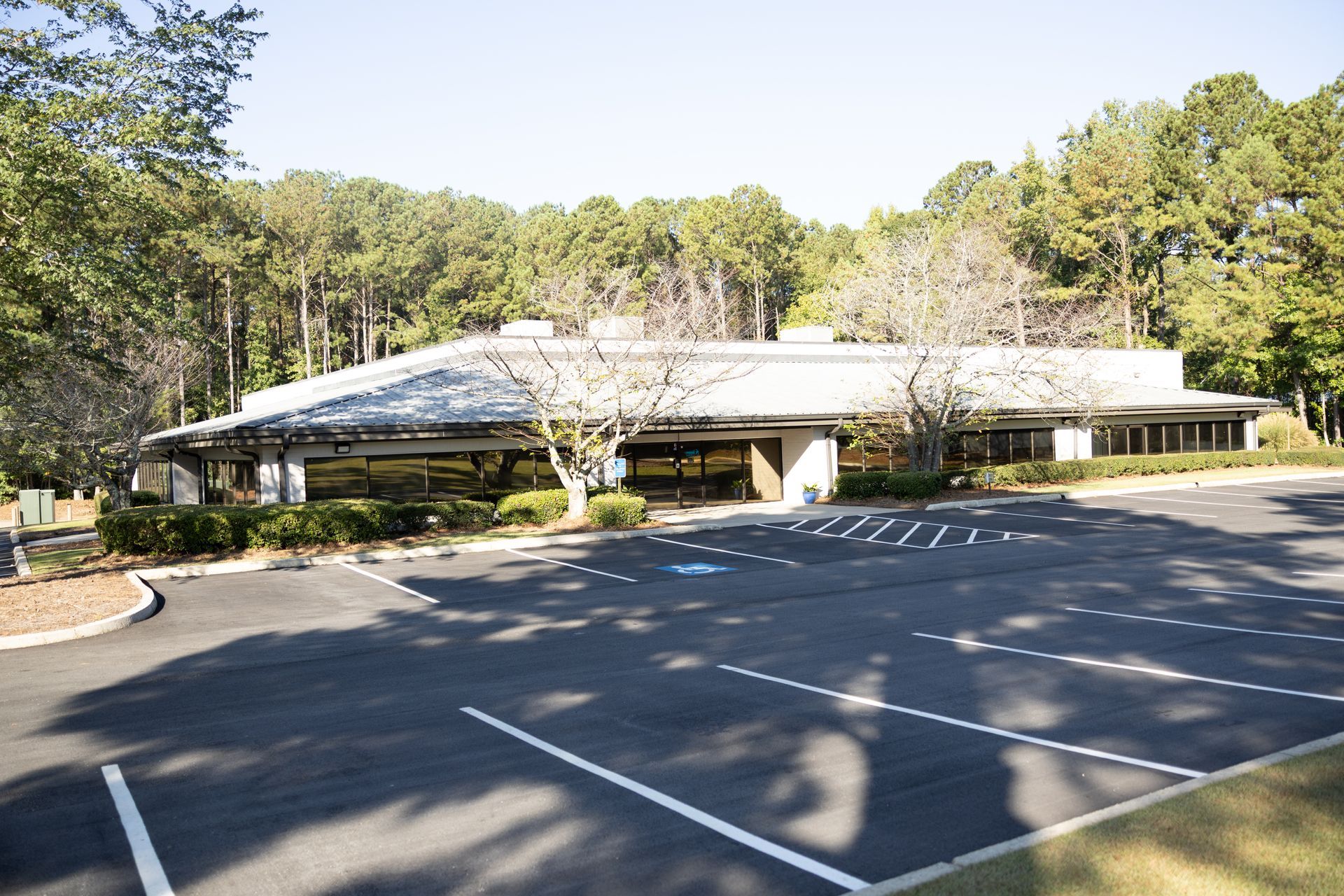 Building with a flat roof and surrounding parking lot, set against a backdrop of trees.