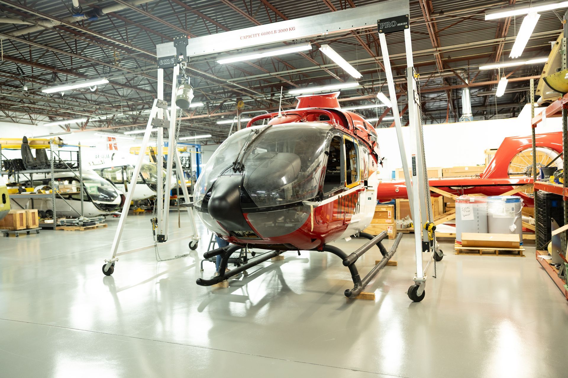 Red and white helicopter inside a hangar, supported by a gantry crane.
