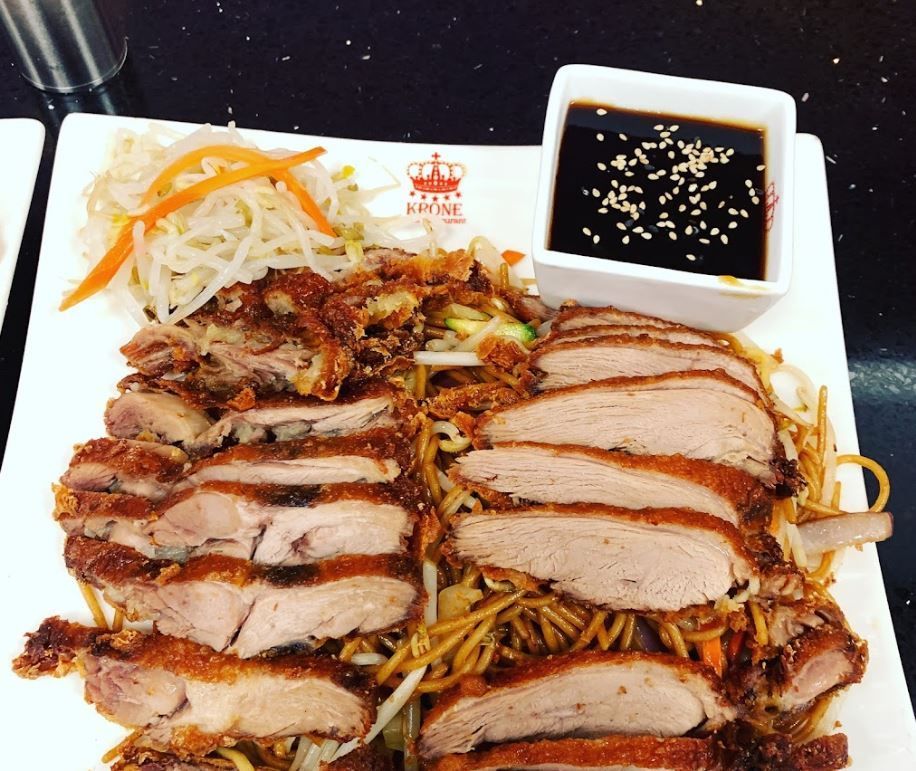 ein weißer Teller mit Fleisch und Nudeln und einer Schüssel Soße