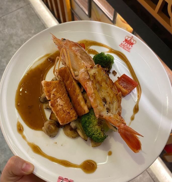 eine Person hält einen Teller mit einem Fisch und Gemüse darauf