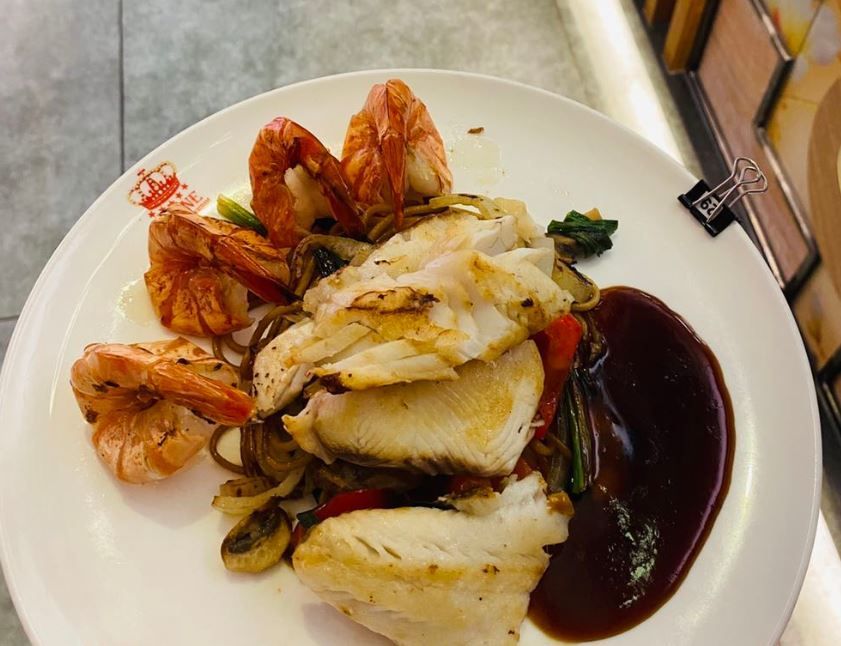 ein weißer Teller mit Fisch und Garnelen auf einem Tisch .