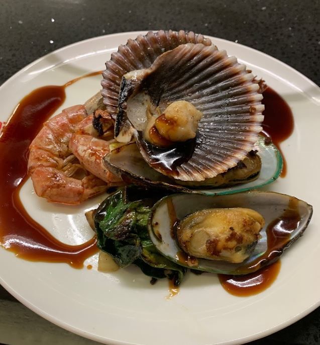 ein weißer Teller mit Meeresfrüchten und Soße darauf