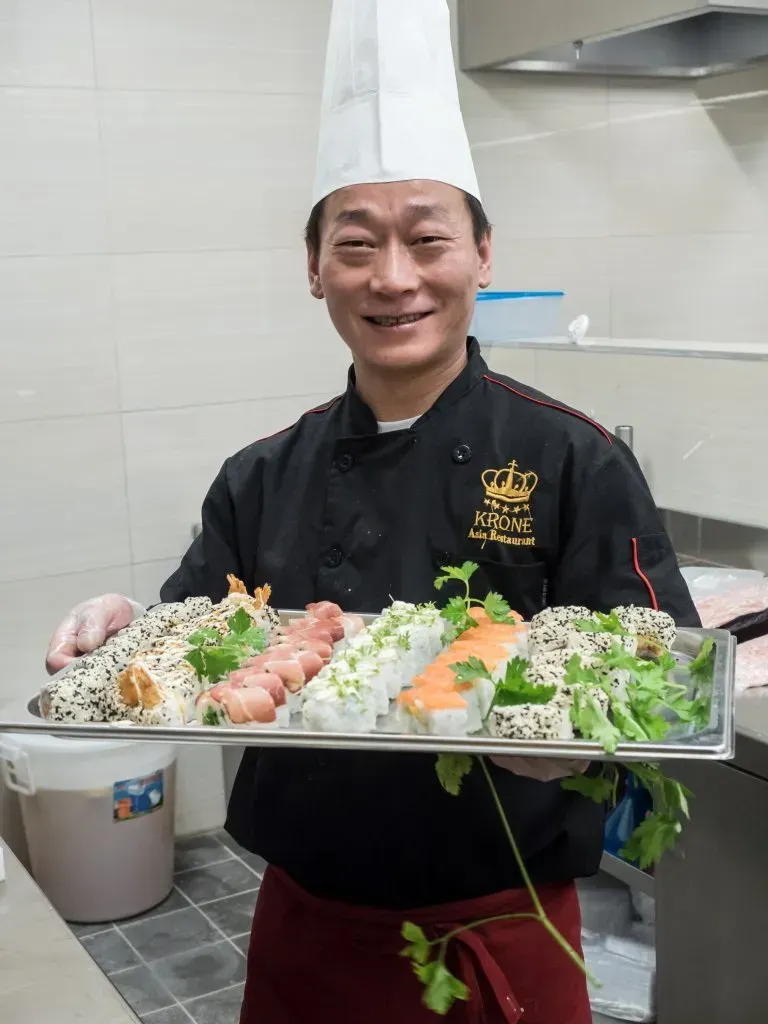 ein Koch hält ein Tablett mit Sushi in einer Küche .