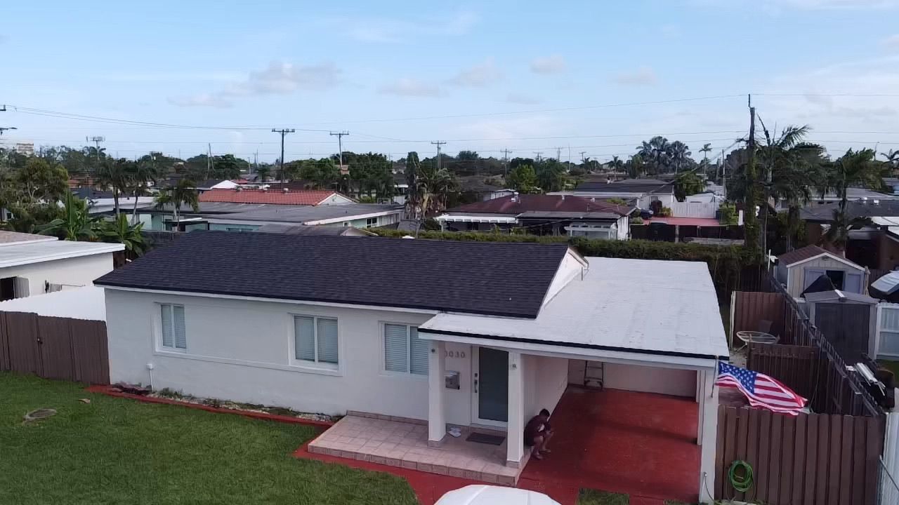 An aerial view of a white house with a black roof in a residential area.