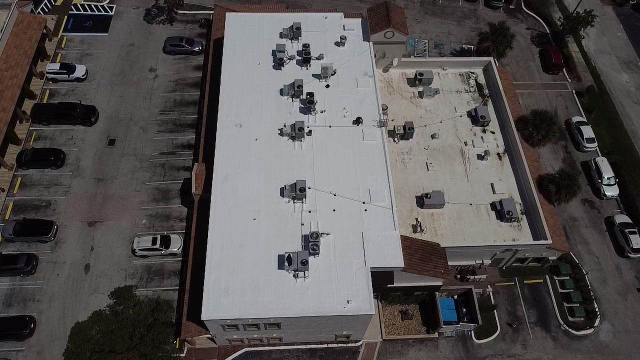 An aerial view of a building with a white roof and a parking lot.