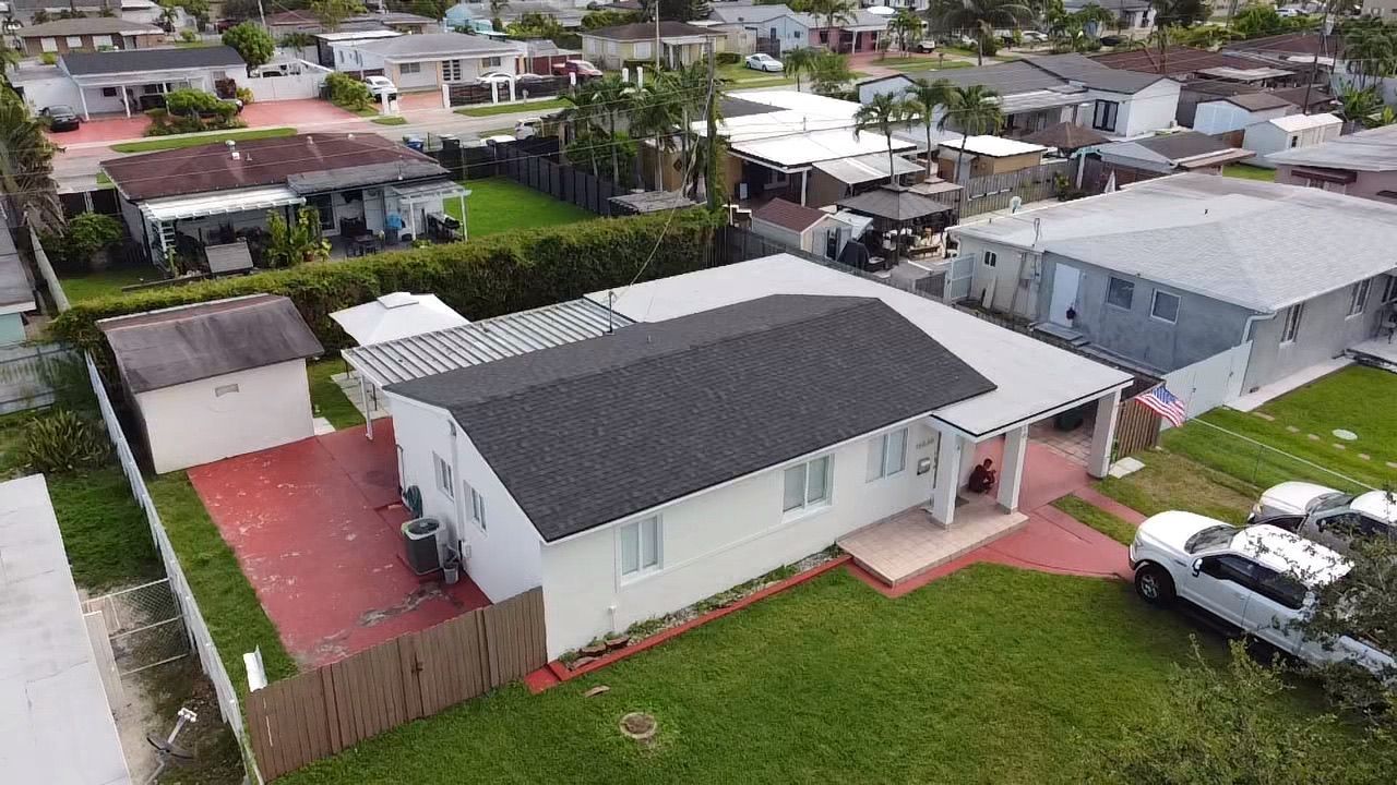An aerial view of a house in a residential area with cars parked in front of it.