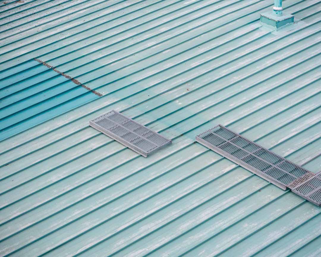 An aerial view of a green metal roof with two vents on it.