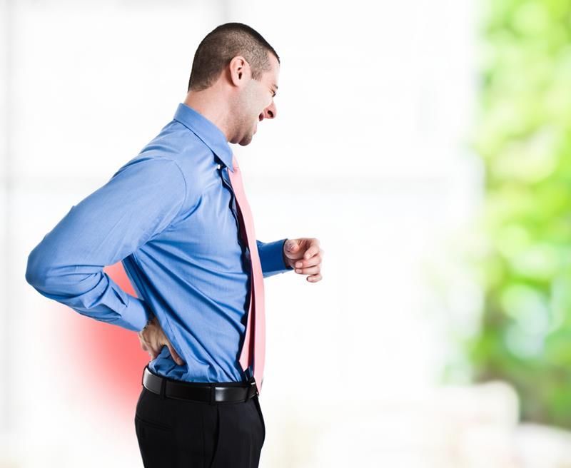 Man in business attire clutching his lower back in pain; red area highlights the pain; blurry background.