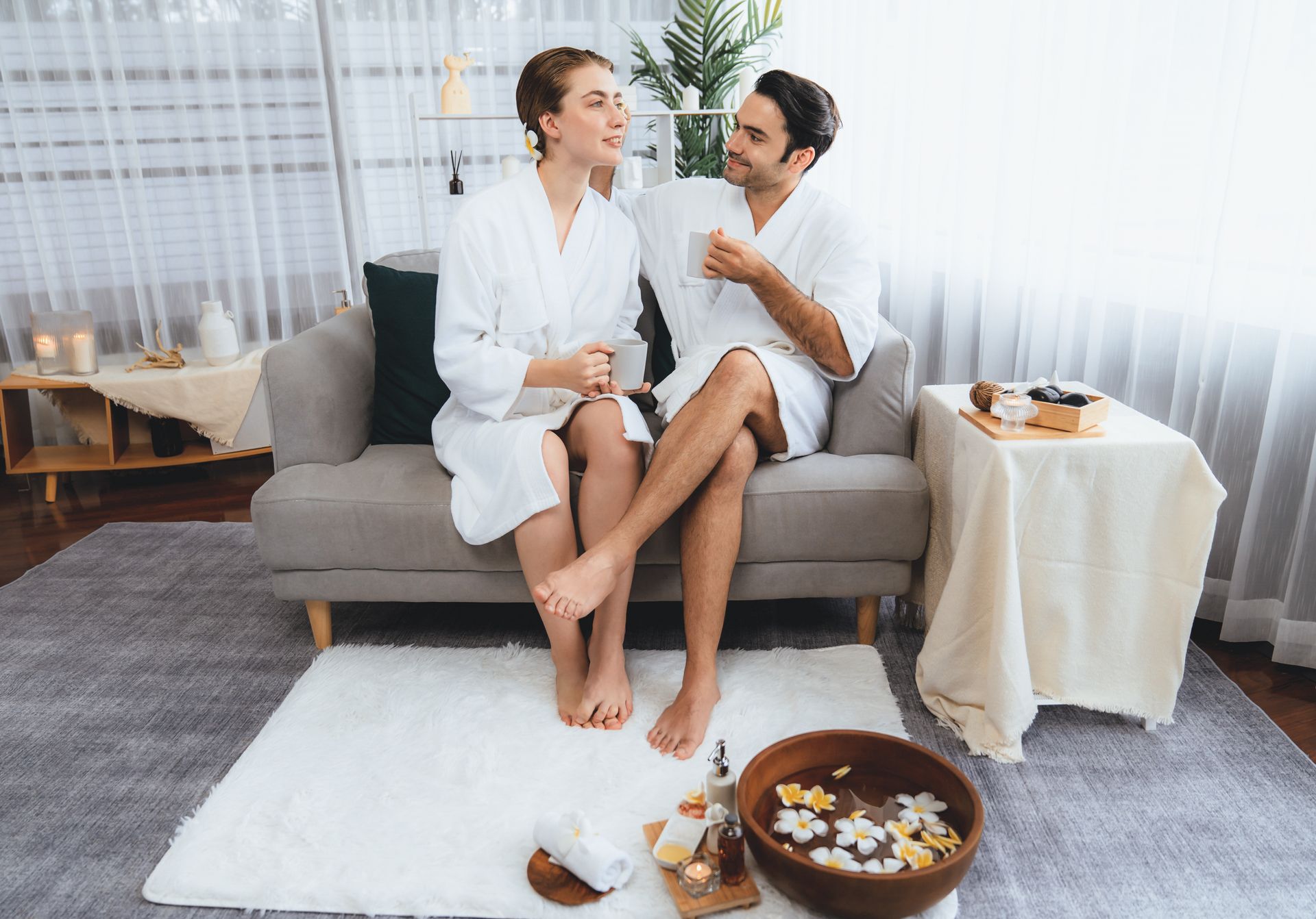 A man and a woman are sitting on a couch drinking tea and enjoying an at-home spa.