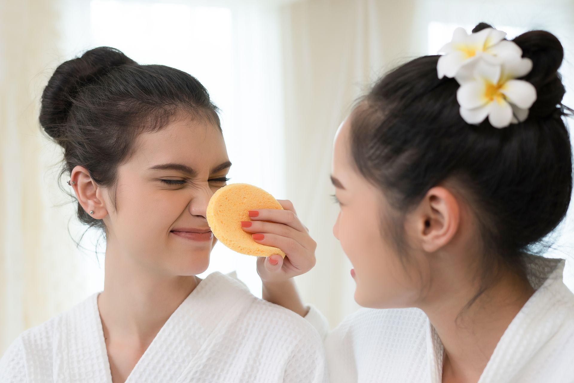 Two women are cleaning their faces with a sponge.