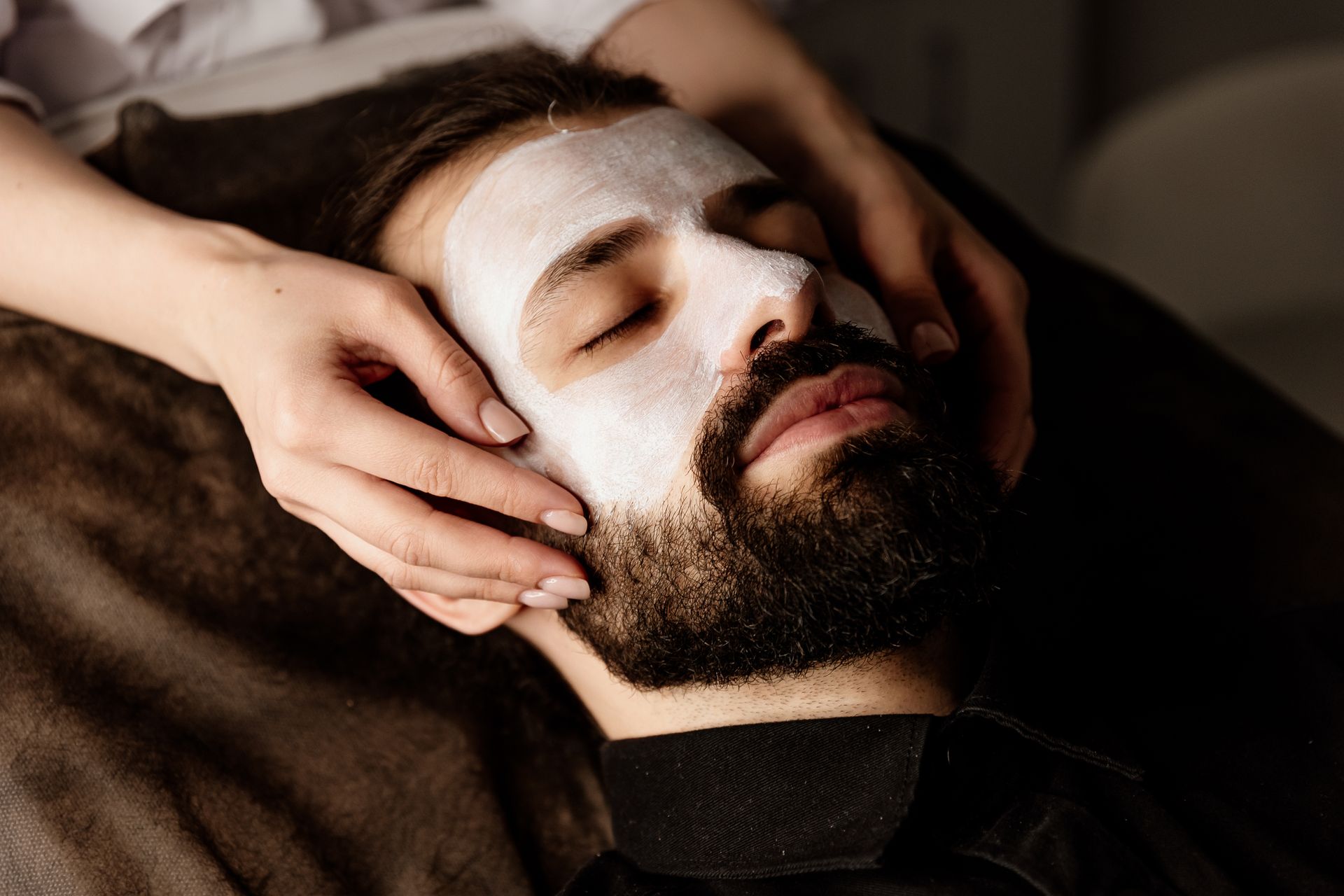 A man with a beard is getting a white mask on his face.