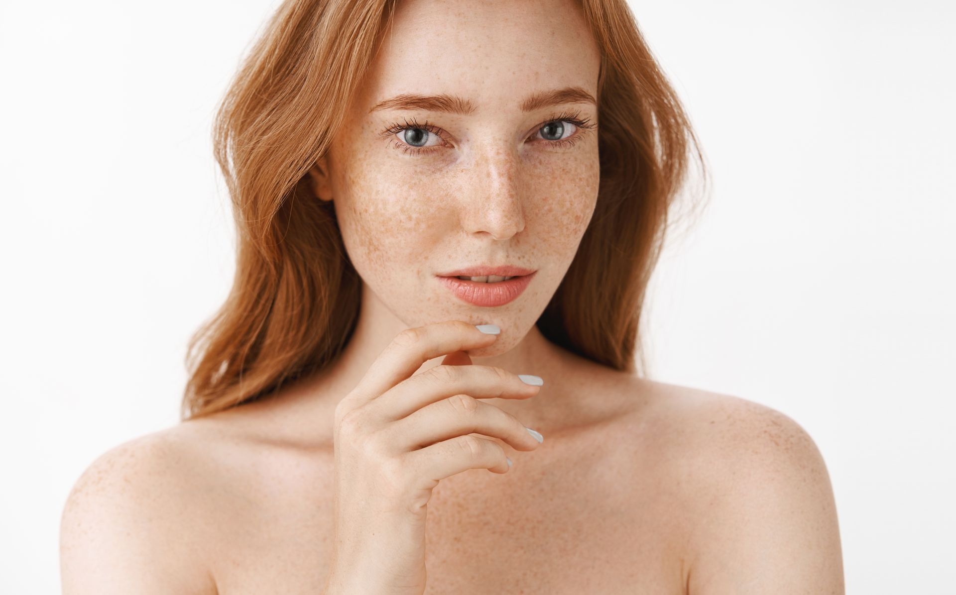 A woman with red hair and freckles is touching her face.