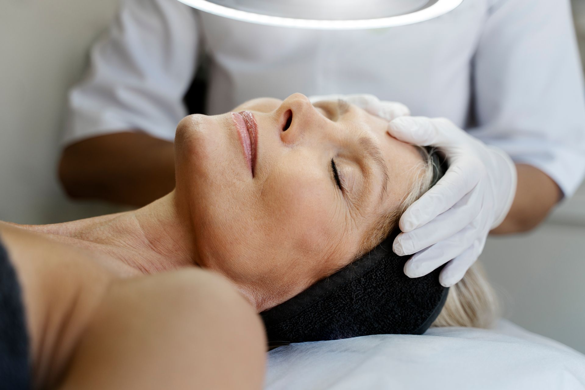 Spa therapist giving a facial massage to a relaxed client lying on a treatment bed