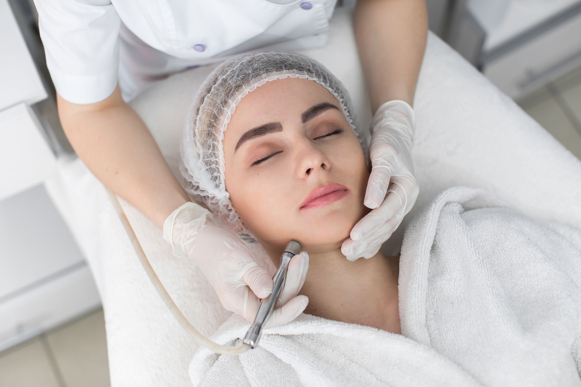 Aesthetic facial treatment on a woman with closed eyes in a white spa setting