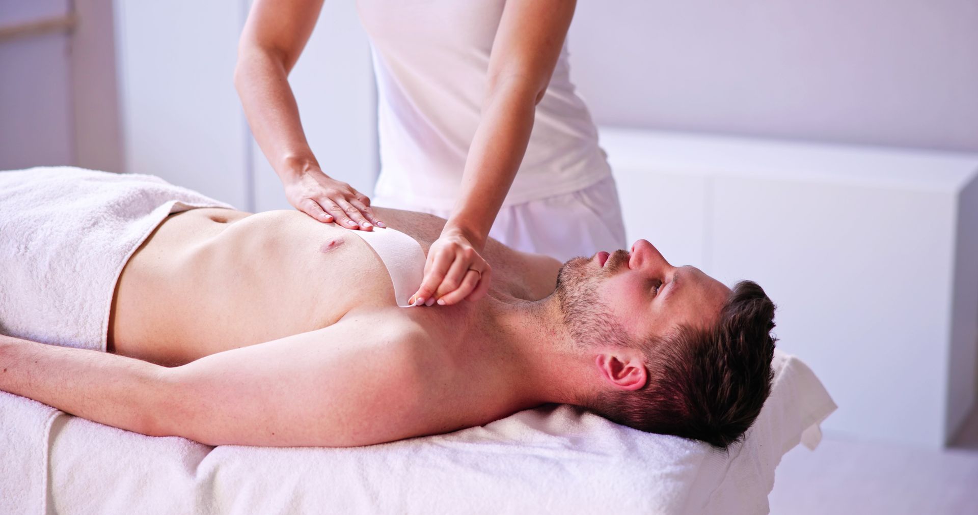 Man receiving chest massage from a person in white clothing; indoors.