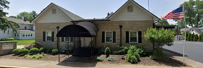 Stone building with white gabled roofs, black shutters, and a covered entrance.