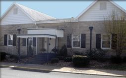 Stone building with white gabled roofs, black shutters, and a covered entrance.