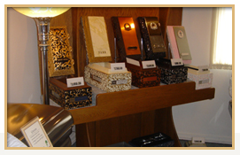 Wooden display shelf with various rectangular boxes, likely for urns, in a brightly lit room.