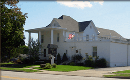 White building with porch and American flag; likely a funeral home.