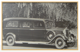 Black hearse parked on a road, trees in the background.