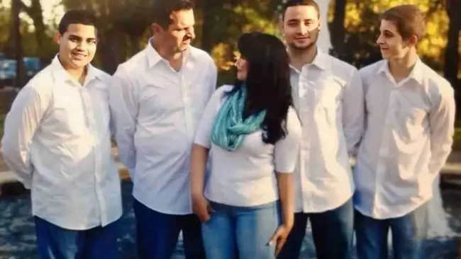 Family of five, all in white shirts and blue jeans, pose near water.