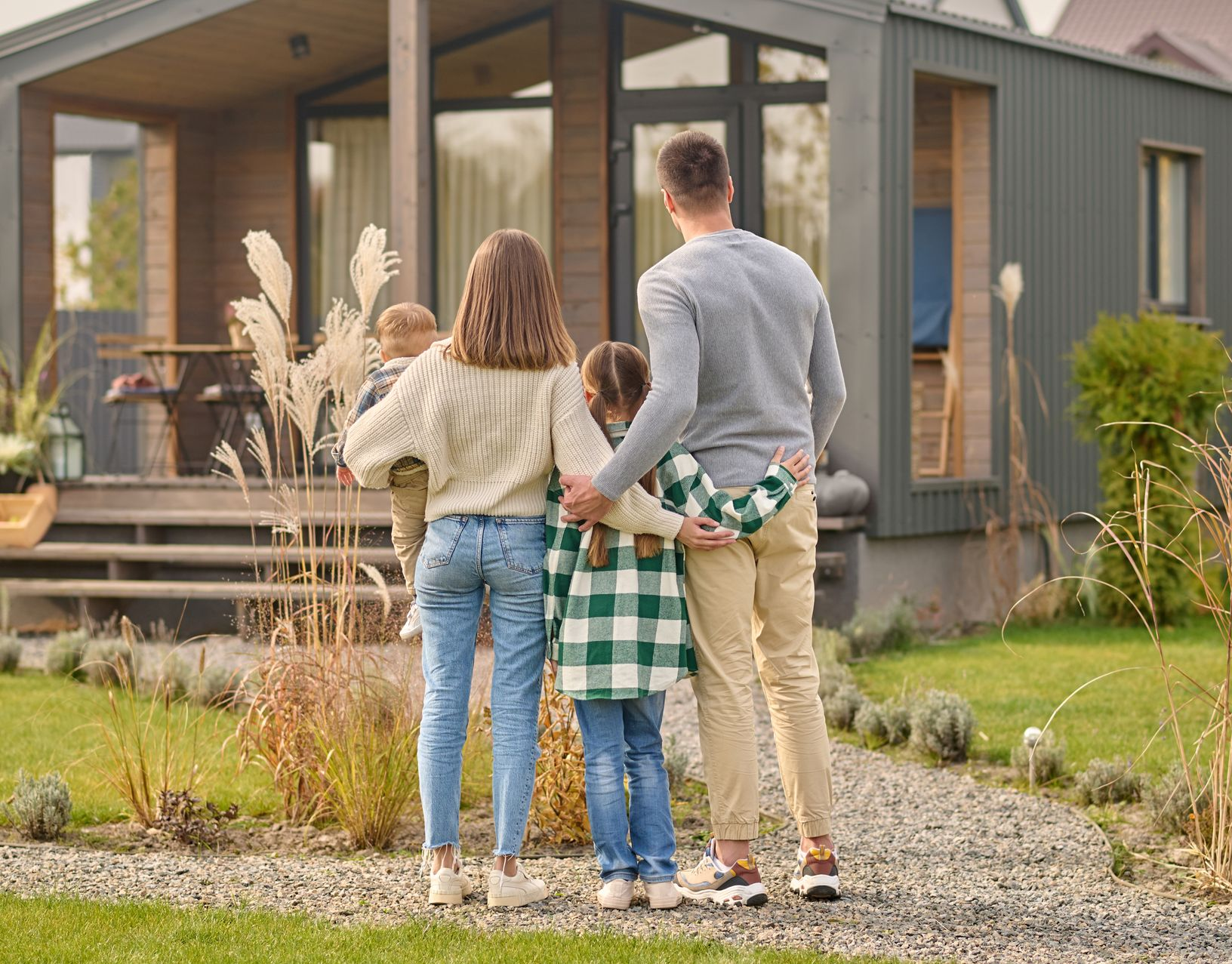 Family of four stands in front of a modern house, looking towards the entrance.