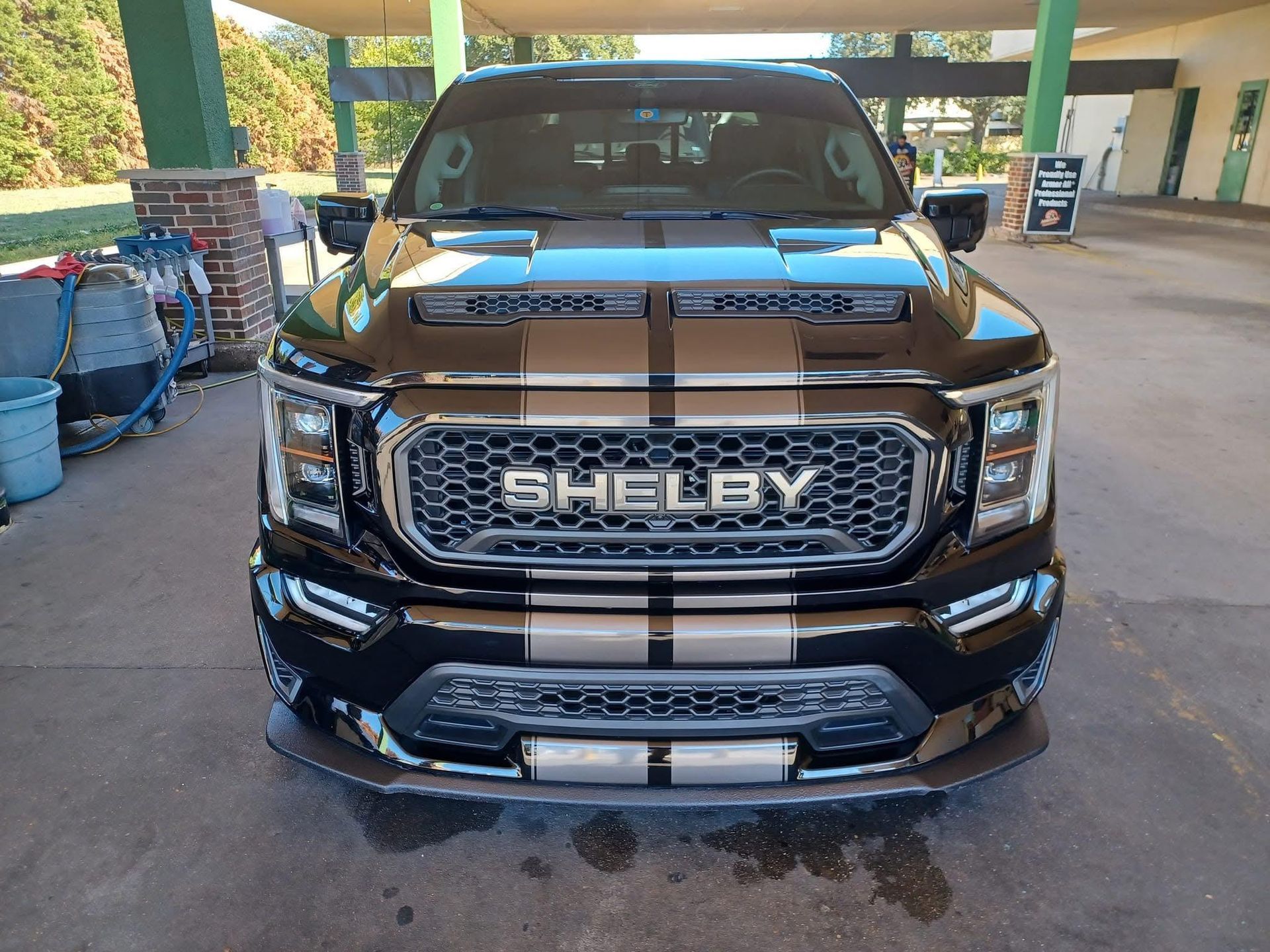 Black Shelby Ford truck with silver racing stripes, parked in a car wash. 