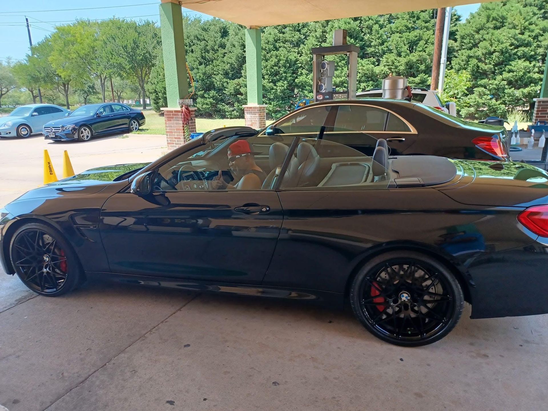 Black convertible car parked at an outdoor station with a person in the driver's seat.
