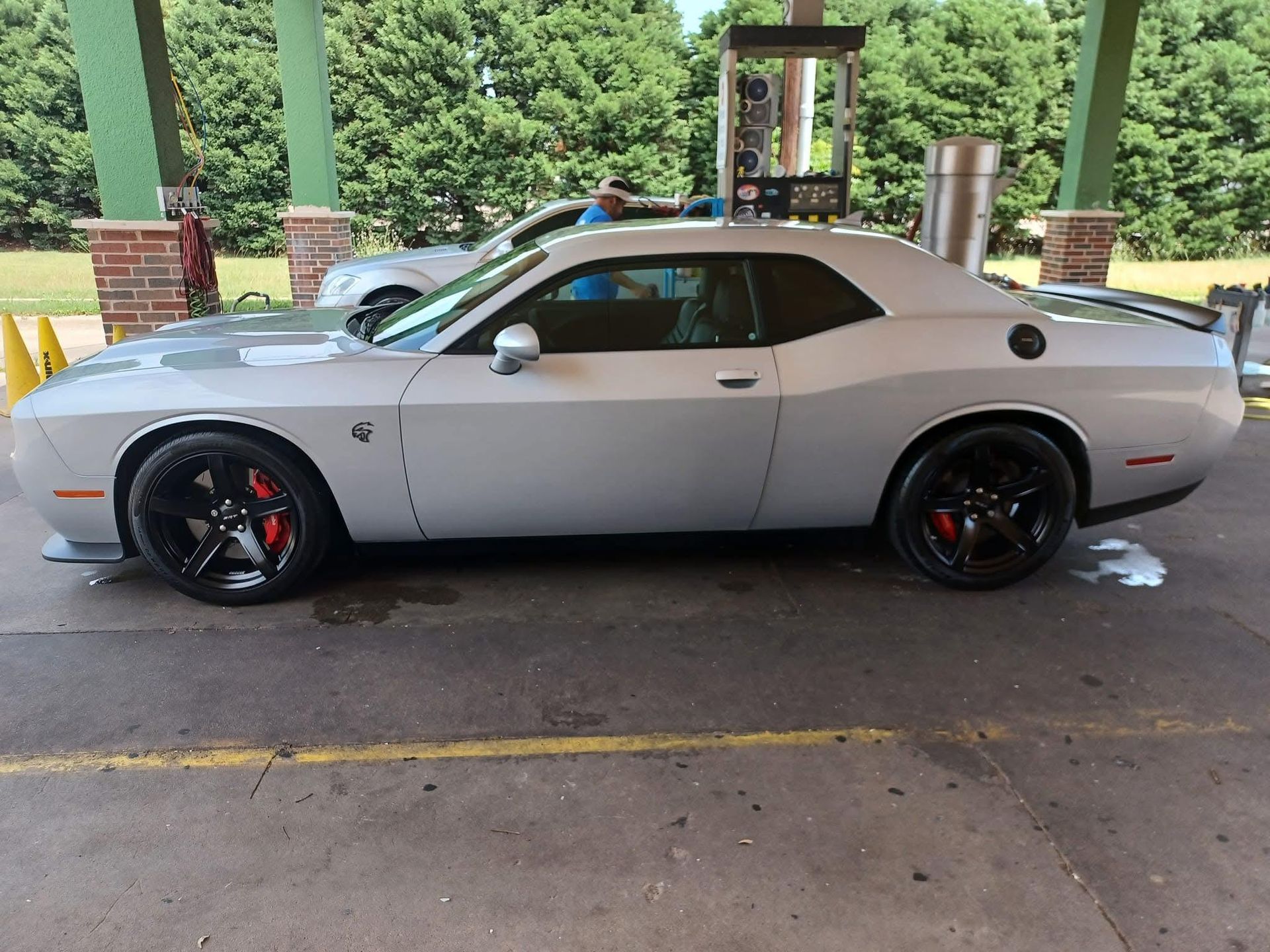 Silver Dodge Challenger at a car wash, with black wheels and red brake calipers. The setting is outdoors.
