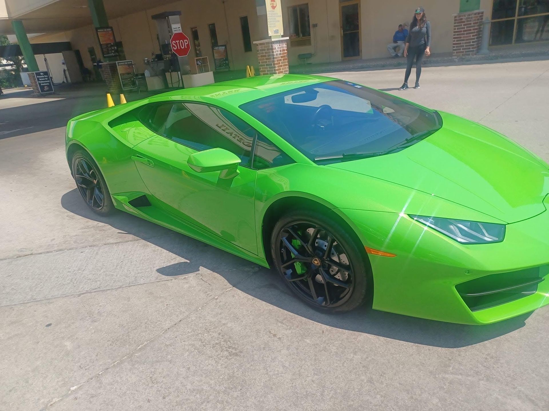 Bright green Lamborghini sports car parked on a paved surface, with a person standing nearby.