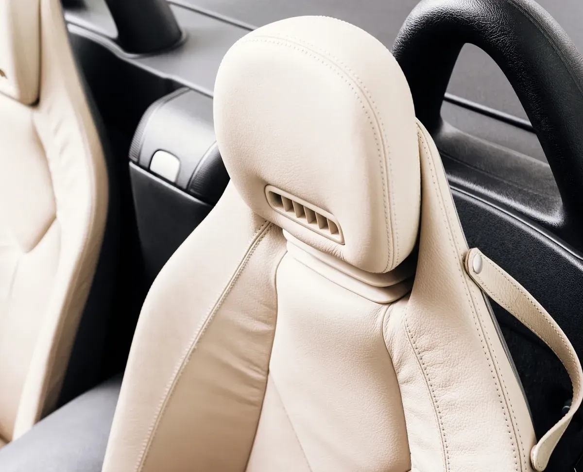 Beige car seat with headrest, seatbelt, and black details, likely in a convertible.
