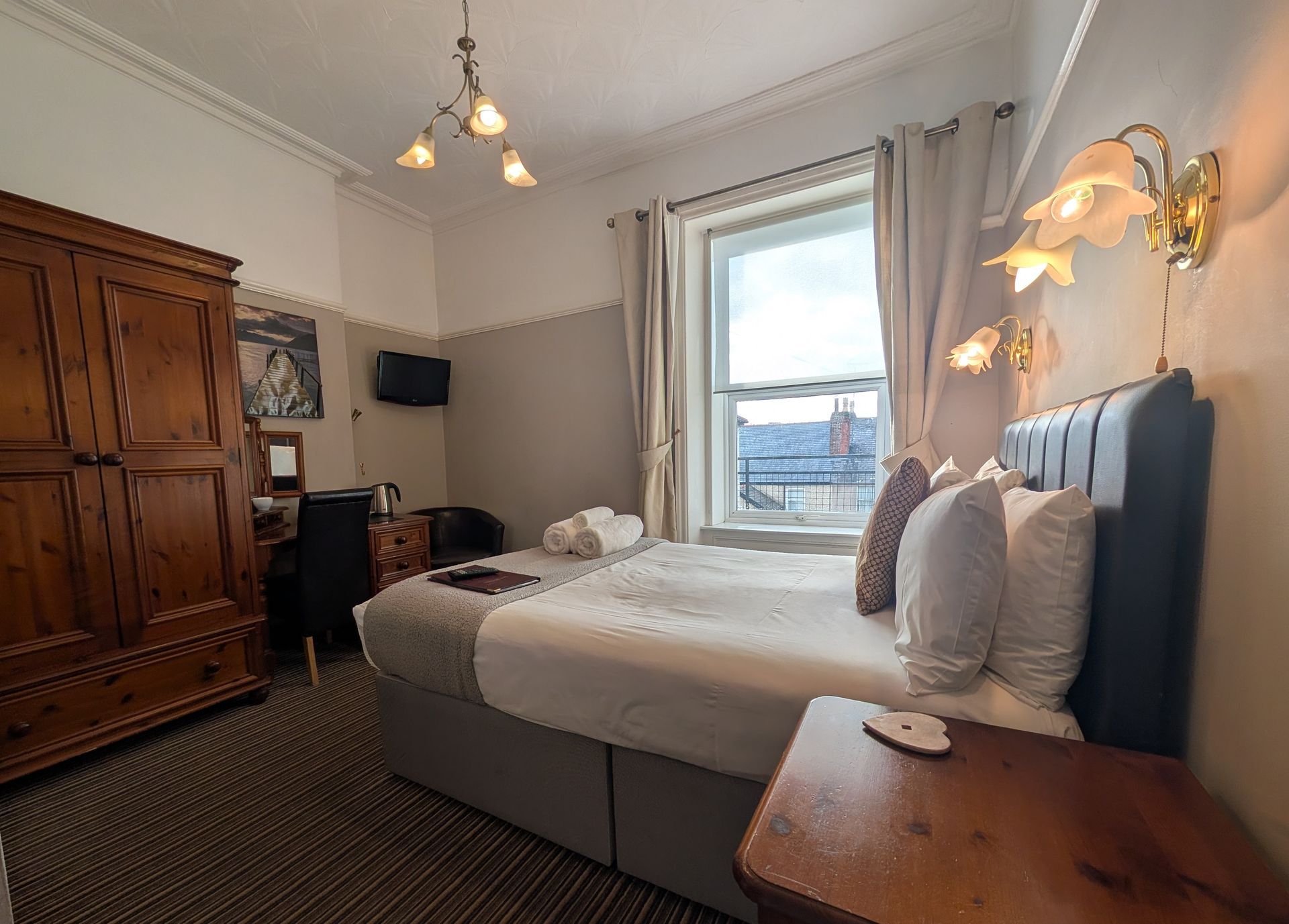 Bedroom with bed, wardrobe, desk, window, and sconce lights.