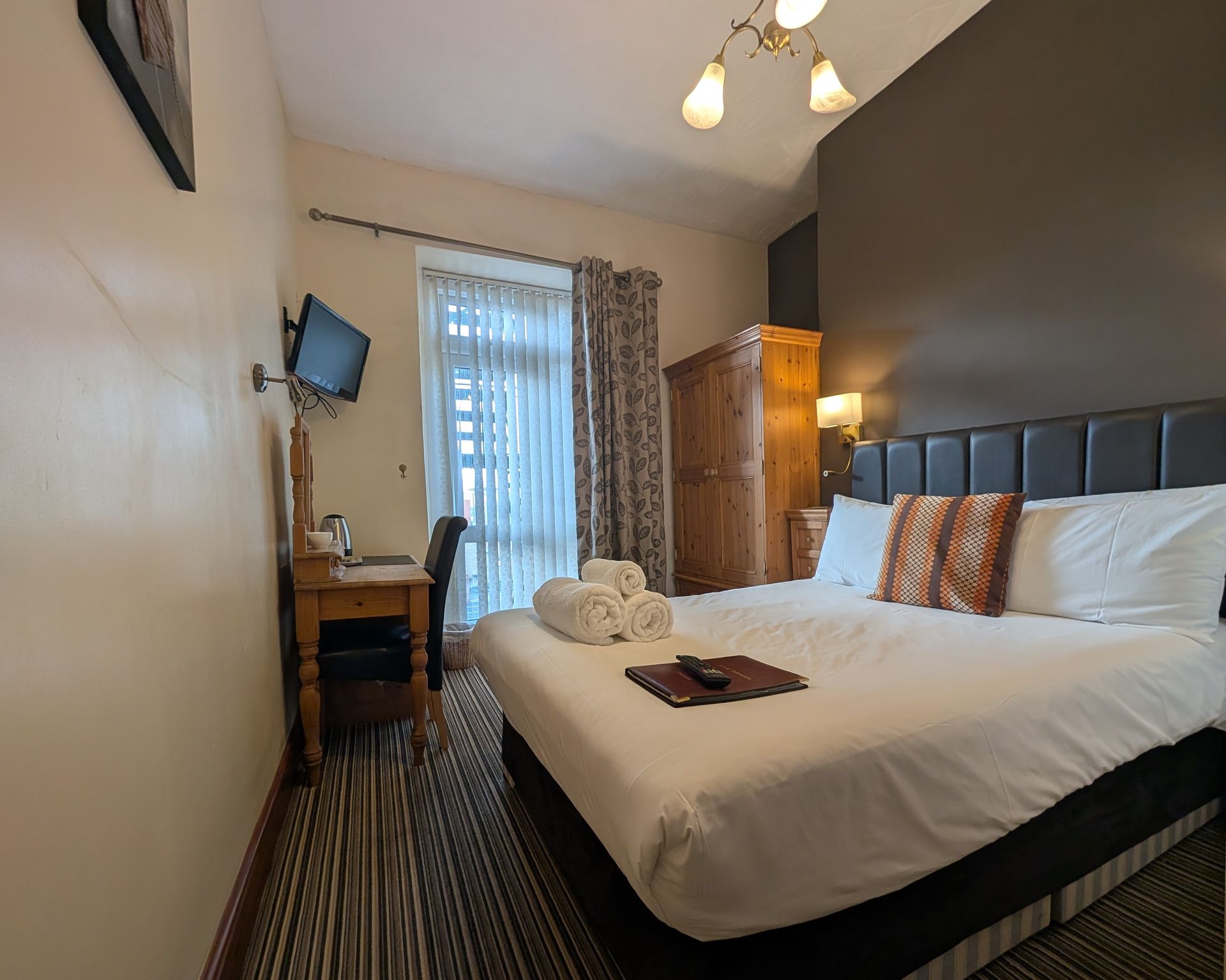 Bedroom with a large bed, wooden furniture, a small desk, and a window with curtains.
