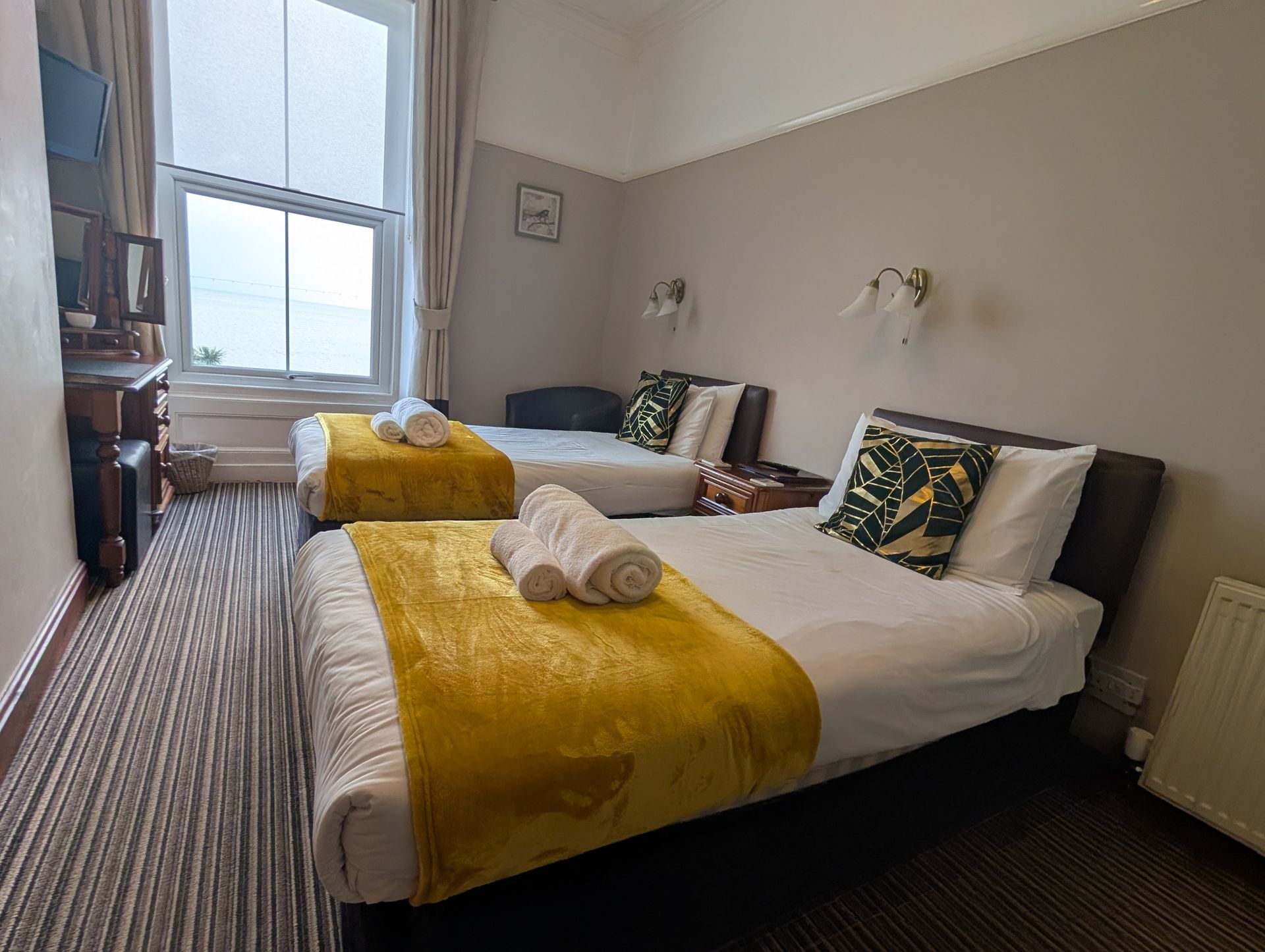 Twin hotel room with two beds, yellow blankets, a window, and a dresser.