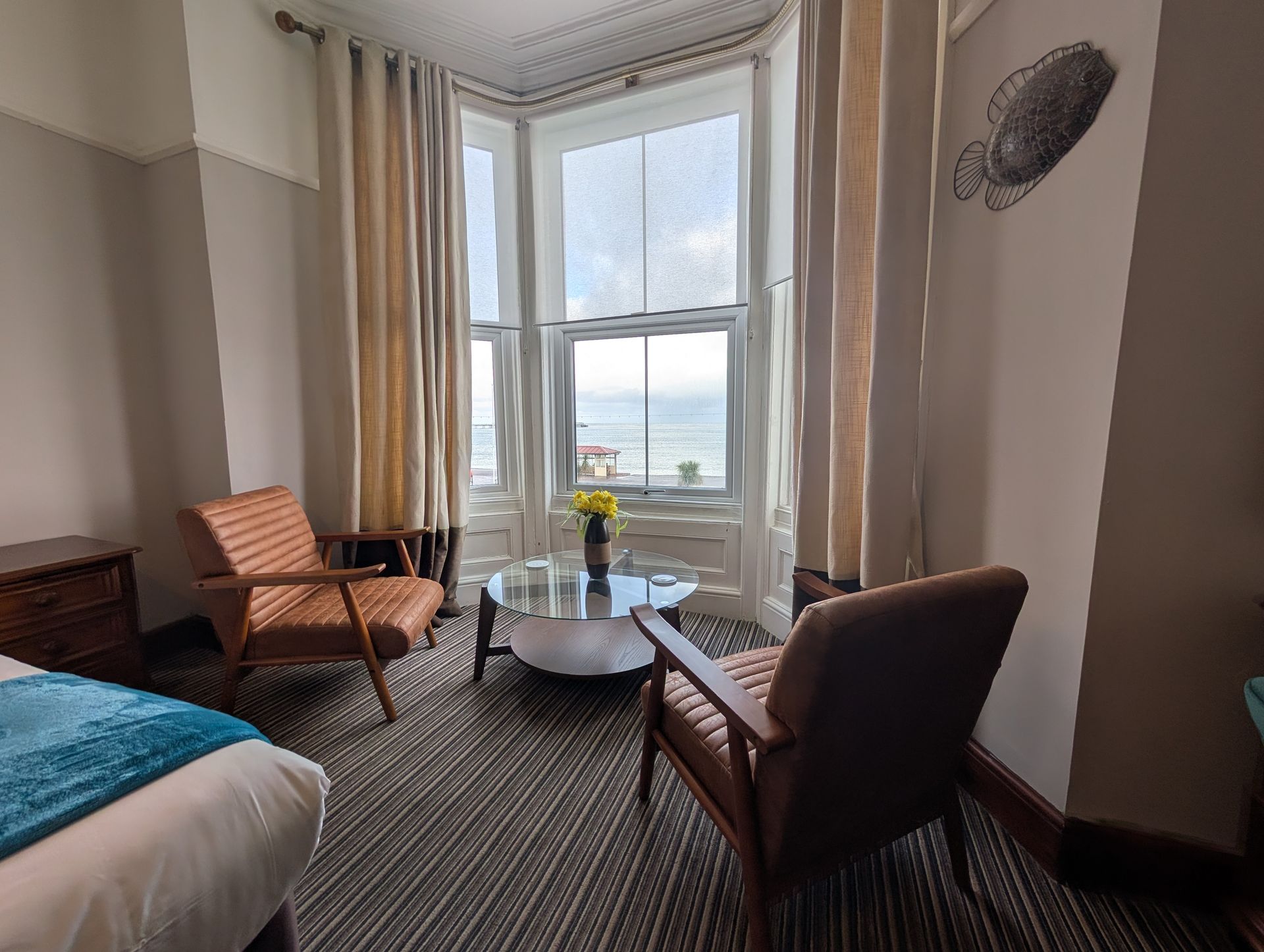 Cozy room with bay window, two mid-century chairs, round table, ocean view, and light-colored curtains.