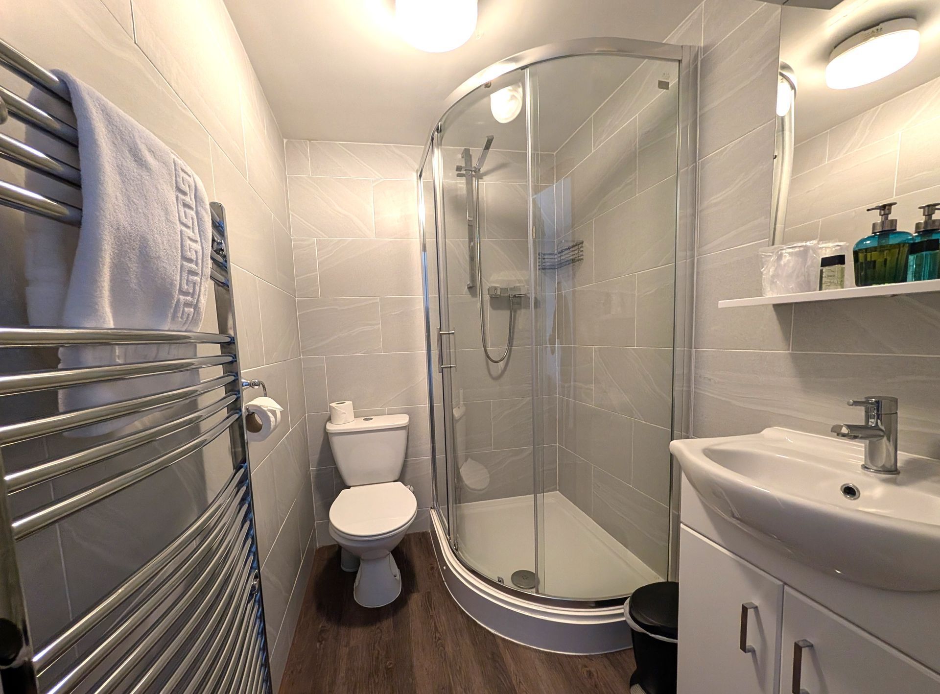 Small modern bathroom with a shower, toilet, and sink. Towel on a radiator.