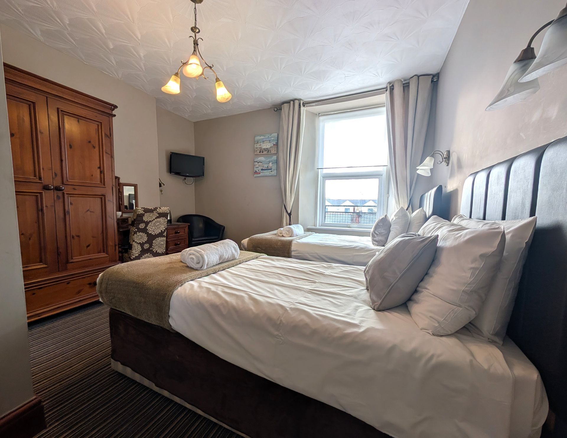 Bedroom with two beds, large wooden wardrobe, window with curtains, and small TV.