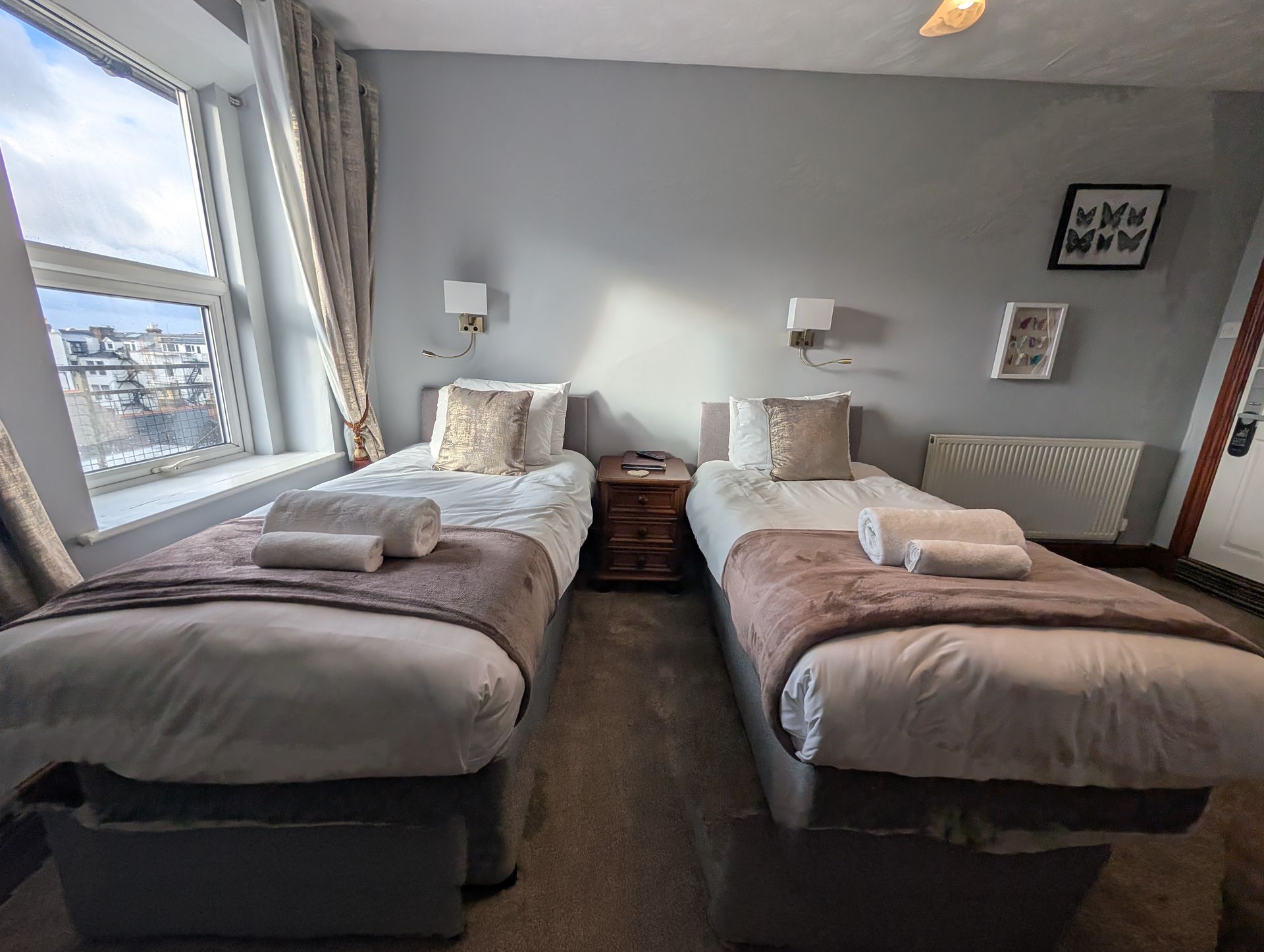 Twin beds in a bedroom with gray walls, a window, and a nightstand.