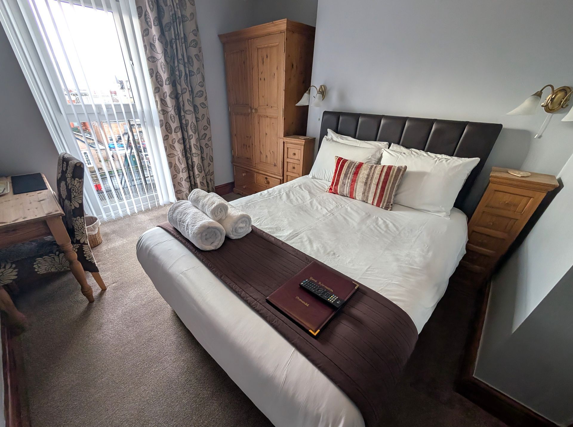 Bedroom with a bed, nightstands, wardrobe, a desk, and a balcony. White linens, dark brown accents.