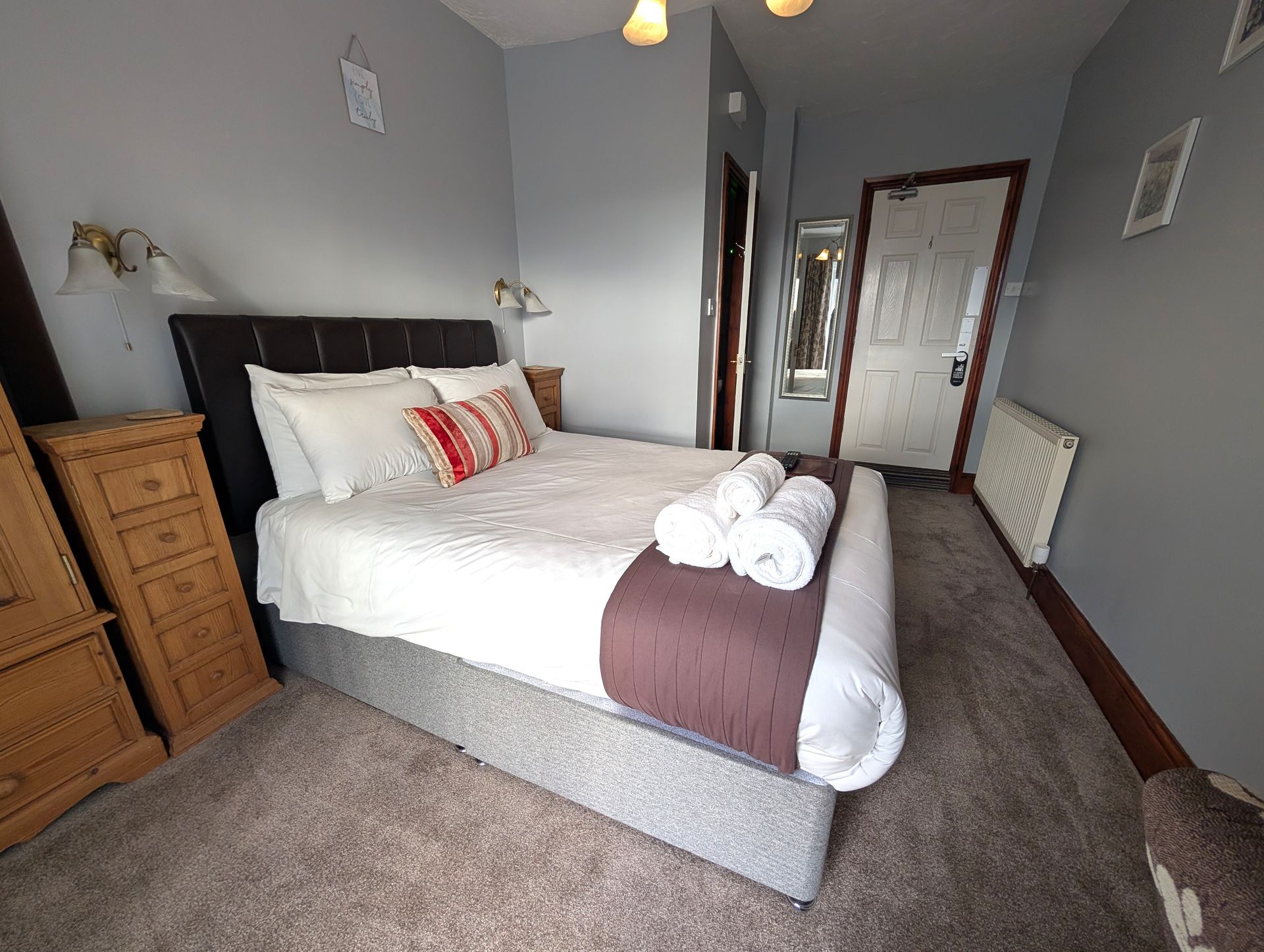 Bedroom with bed, nightstands, and closed door; light gray walls, brown carpet.