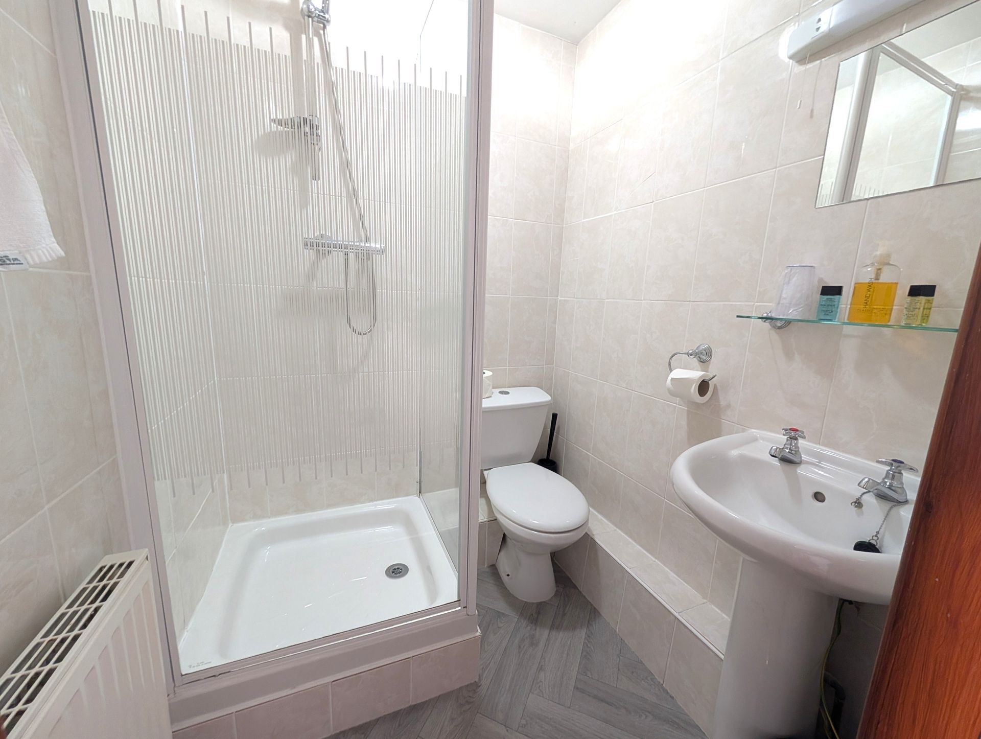 Bathroom with a white shower, toilet, and sink. Beige tiled walls.