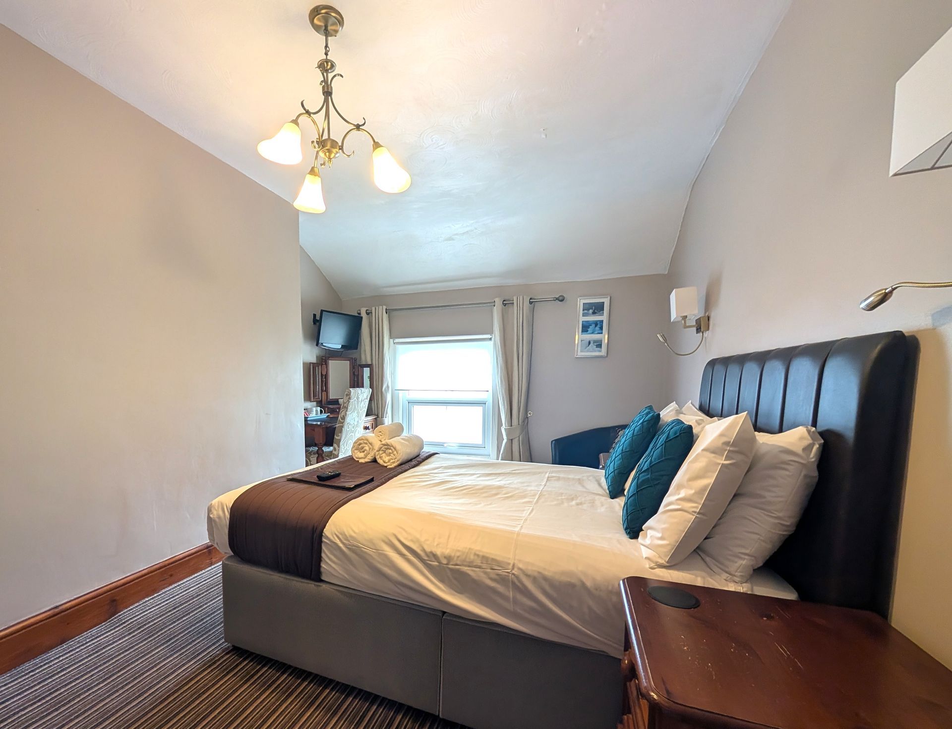 Bedroom with bed, nightstand, window, TV, and decorative chandelier.