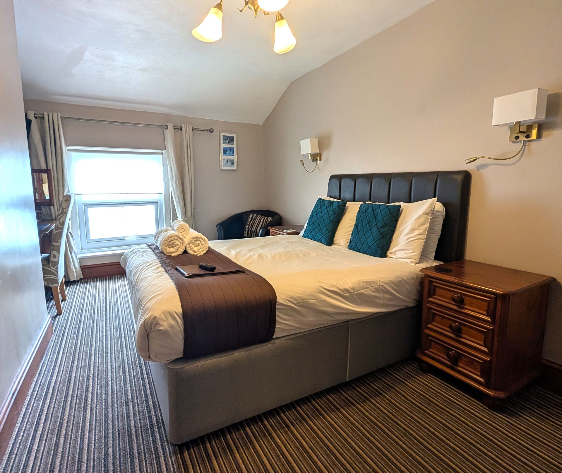 Bedroom with a bed, nightstand, window, and small sitting area; neutral colors.