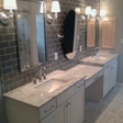 Bathroom with white cabinets, gray brick-style tile, and three vanity mirrors with sconces.