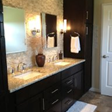 Bathroom with dark cabinets, light granite countertop, two sinks, and a beige tile backsplash.