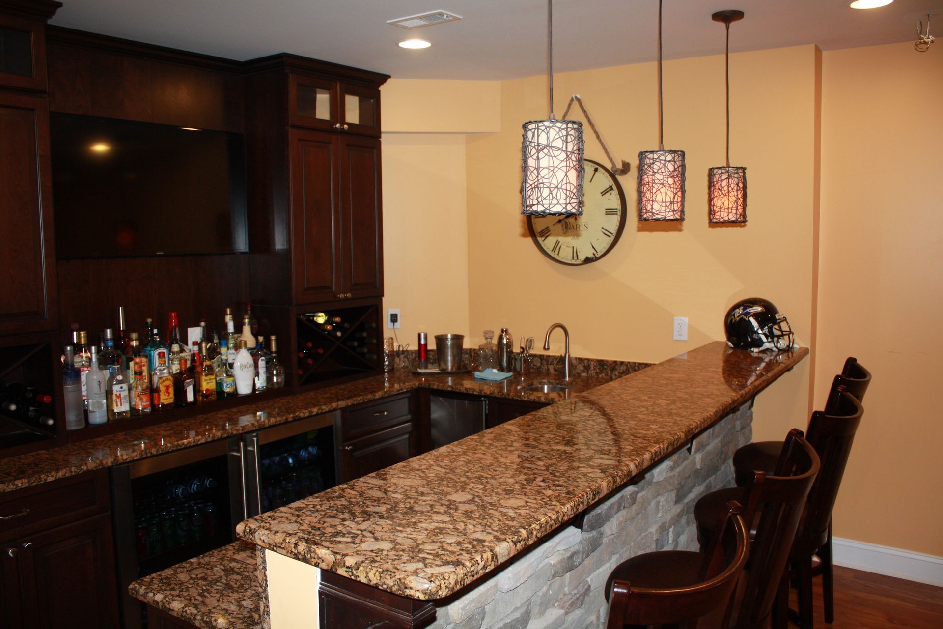 Upscale home bar with dark cabinetry, granite countertops, and pendant lights.